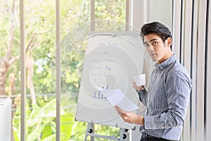 Business and Comminication Concept. Asian young businessman standing looking to camera with holding a white cup of hot coffee and