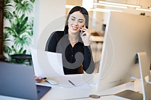 Business, communication and people concept. Happy businesswoman with laptop computer and papers calling on desk phone at office