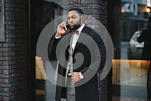 Business communications. Happy young African man in formal wear talking on the mobile phone and smiling while standing outdoors