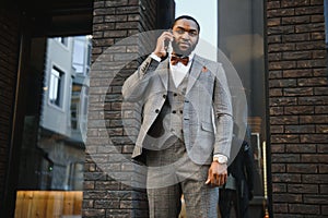 Business communications. Happy young African man in formal wear talking on the mobile phone and smiling while standing outdoors