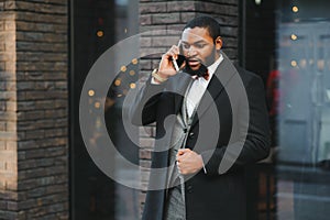 Business communications. Happy young African man in formal wear talking on the mobile phone and smiling while standing outdoors