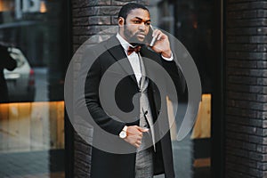 Business communications. Happy young African man in formal wear talking on the mobile phone and smiling while standing outdoors