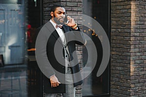 Business communications. Happy young African man in formal wear talking on the mobile phone and smiling while standing outdoors