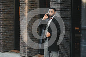 Business communications. Happy young African man in formal wear talking on the mobile phone and smiling while standing outdoors