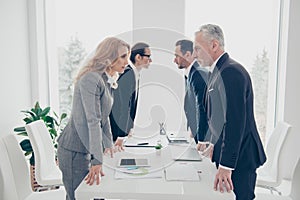 Business competition, four stylish business persons in suits having disagreement and conflict, standing together near desktop in