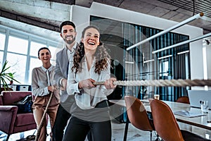 Business competition symbol. Group of young smiling office workers playing tug of war