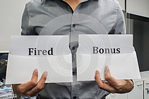 Business concept - businessman hold fired and bonus sign for work performance