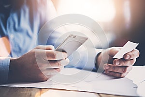 Business concept. Businessman holding hand white businesscard and making photo smartphone. New work project on the table