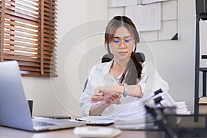 Business concept, Businesswoman is look at the time on the wristwatch after working hard in office