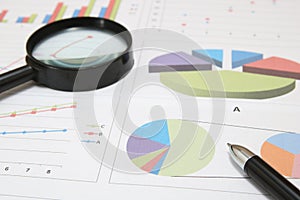 Business concept. Charts, diagrams, tables with pen and magnifying glass.