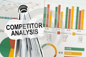 On the business charts there is a notebook on which there is a paper plate with the inscription - Competitor Analysis