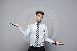 Business Concept - Confident thoughtful young African American showing balancing hands on side over grey background.