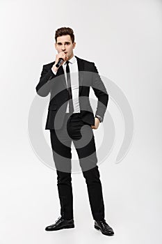 Business Concept: Full-length Portrait young man in black suit is holding a microphone, singing and posing against a