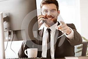 Business concept. Happy smiling young businessman sitting in office talking on a cell phone getting good news about his