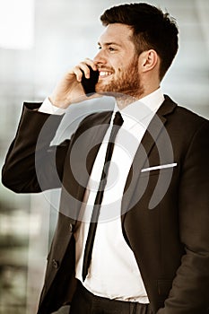 Business concept. Happy smiling young businessman standing in office talking on a cell phone getting good news about his