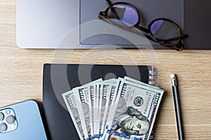 Business concept. Laptop, banknotes of us dollars, business card holder, smart phone and opened Notepad with pen. Top view of the