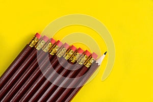Business concept - lot of same pencils and one different pencil on yellow paper background. It`s symbol of leadership, teamwork.