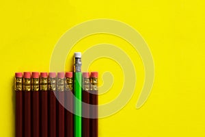 Business concept - lot of same pencils and one different pencil on yellow paper background. It`s symbol of leadership, teamwork.