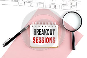 Business concept. Notebook with text BREAKOUT SESSION on pink paper with magnifier, keyboard and pen in the white background