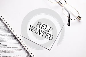 Business concept. Notebook with text Help Wanted sheet of white paper for notes and glasses in the grey background