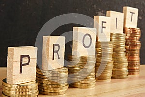 Business concept with PROFIT word on wooden plate onto hike trend stacked of coins.