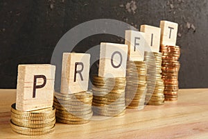 Business concept with PROFIT word on wooden plate onto hike trend stacked of coins.