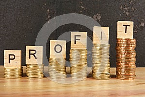 Business concept with PROFIT word on wooden plate onto hike trend stacked of coins.