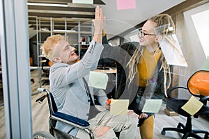 Business concept, successful disabled people at work. Happy successful young man in wheelchair giving a high five to his