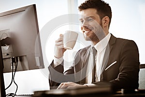 Business concept. Successful young businessman at work. Manager sitting at the office table happy drinking coffee from