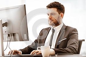 Business concept. Successful young businessman at work. Manager sitting at the office table and working on computer