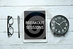 Business concept. Top view of glasses,pen,clock and tablet written with Breakout Sessions on white wooden background.