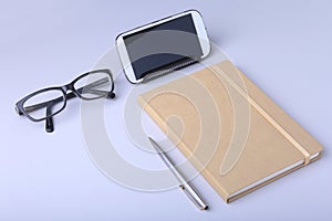 Business concept. Top view of kraft spiral notebook, glasses, smartphone and black pen isolated on background for mockup.