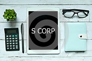 Business concept. Top view of plant,calculator,glasses,pen,notebook and tablet written with S Corp on white wooden background.