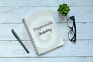 Business concept. Top view of plant,glasses,pen and notebook written with Programmatic Marketing. photo