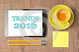 Business concept of trends for 2016 new year. Digital tablet with coffee cup on wooden desk. View from above.