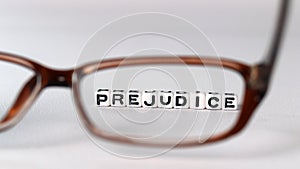 Business concept with white cube arranged in the word  â€™PREJUDICE` and glasses.
