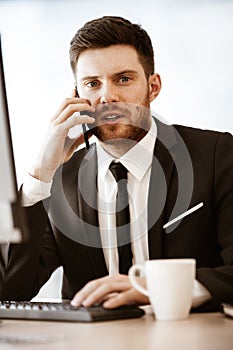 Business concept. Young businessman at the office standing and busy talking on a cell phone resolving a very serious