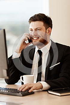 Business concept. Young businessman sitting at the office table happy talking on a cell phone getting good news about