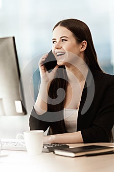 Business concept. Young businesswoman sitting at the office table happy talking on a cell phone getting good news about