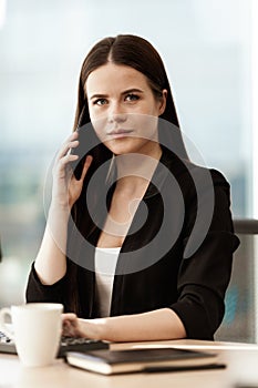 Business concept. Young businesswoman sitting at the office table happy talking on a cell phone getting good news about