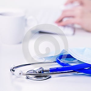 Business concept - Young female doctor woman working at office with computer, typing electronic medical record, white table