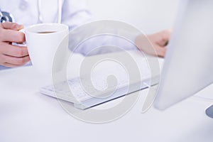 Business concept - Young female doctor woman working at office with computer, typing electronic medical record, white table