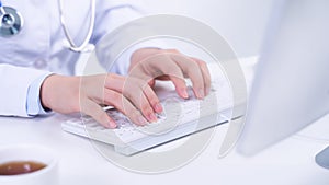 Business concept - Young female doctor woman working at office with computer, typing electronic medical record, white table