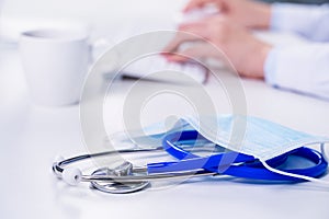 Business concept - Young female doctor woman working at office with computer, typing electronic medical record, white table