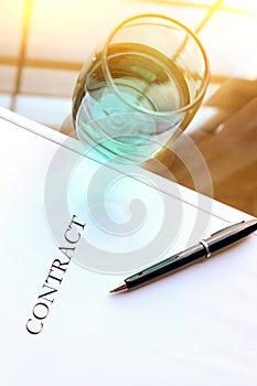 Business contract with pen is ready to sign. A glass of water