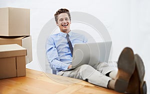 Business couldnt be going better. An excited businessman working on his laptop while surrounded by moving boxes.