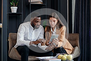 Business couple of african american man and european woman which sitting in specially designated room and using paper