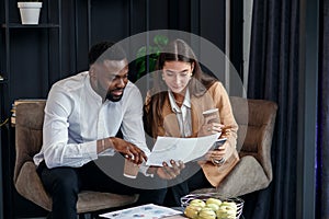 Business couple of african american man and european woman which sitting in specially designated room and using paper