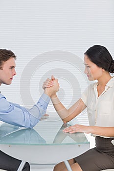 Business couple arm wrestling at desk