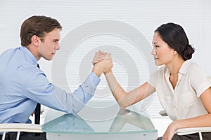 Business couple arm wrestling at desk